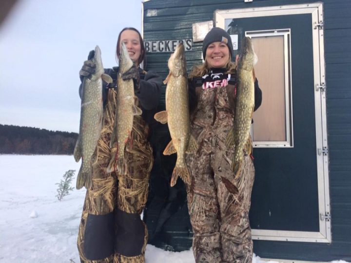 Two women holding large pike fish during ice fishing