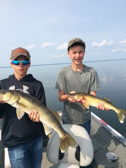 Two boys holding large walleye fish on a boat
