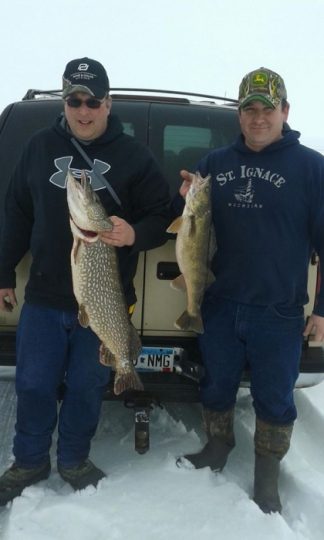 Two men holding large fish caught ice fishing in winter