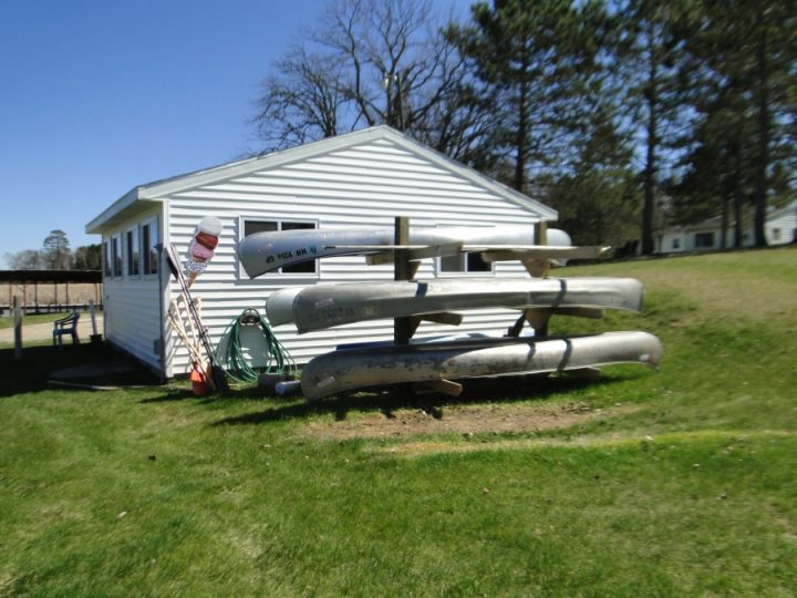 Aluminum canoes stacked on rack beside white building