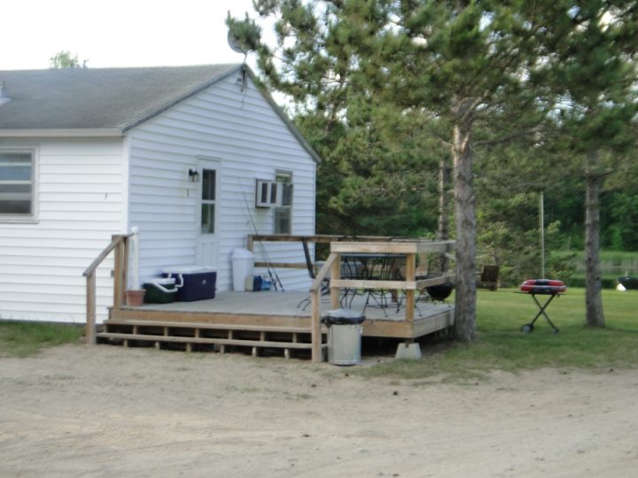 White cottage with wooden deck and grill near pine trees