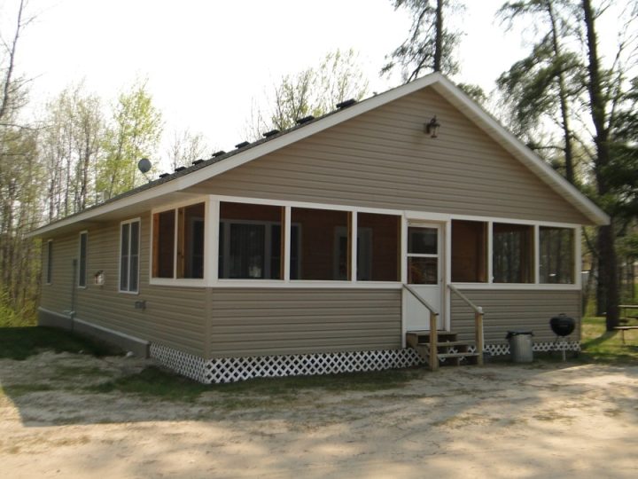 Small tan cottage with screened porch surrounded by trees