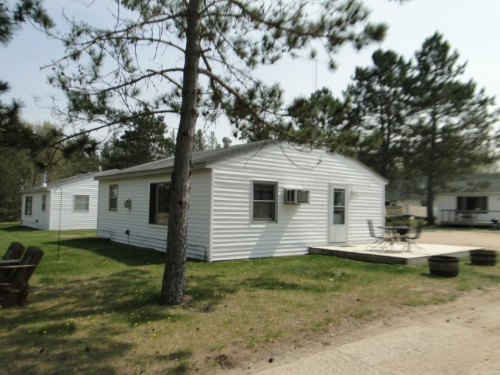 White single-story cottage with deck surrounded by pine trees