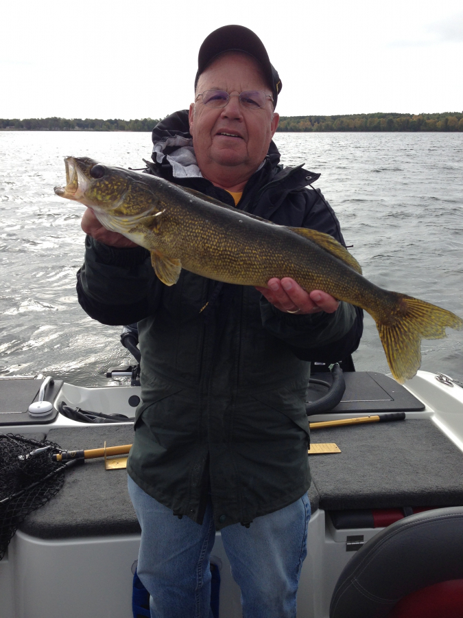 Older man proudly holding a large walleye on a boat