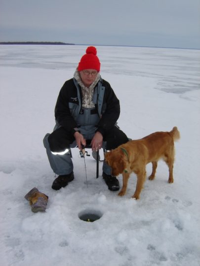 Person ice fishing on frozen lake with golden dog