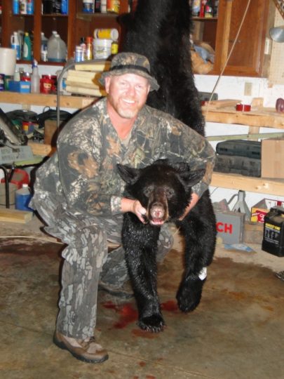 Hunter in camouflage posing with harvested black bear