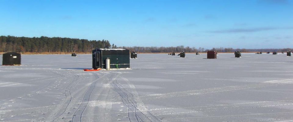 Ice fishing shanties scattered across a frozen lake in winter