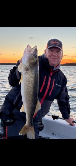 Man holding large walleye fish on boat at sunset