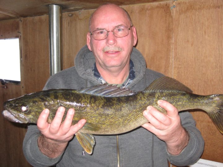 Man proudly holding a large walleye fish inside fishing shack