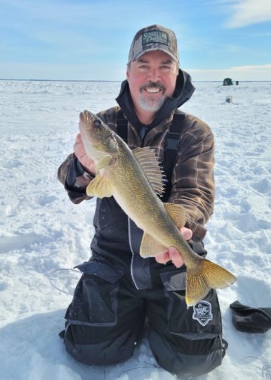 Smiling man holding a walleye fish on frozen lake